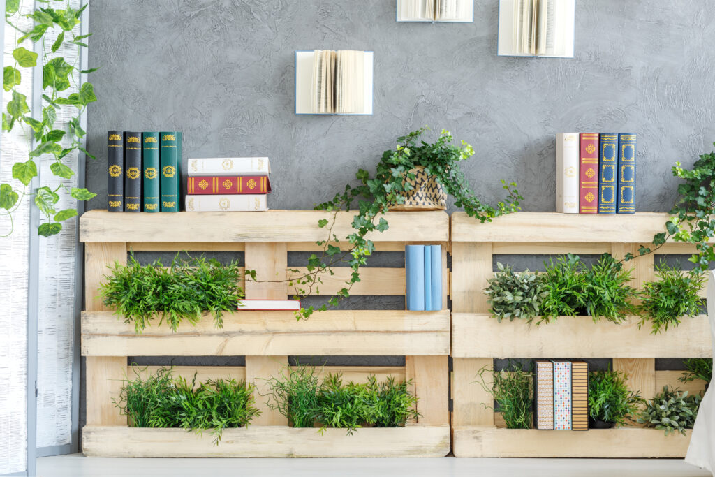 Two pallets being used as modern shelves. The pallets are filled with green plants and beautiful old books. The plants are giving an inviting atmosphere